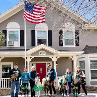 A festive gathering in front of a charming house, featuring a group of people with horses and an American flag waving proudly.