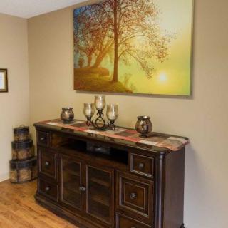 A cozy living room with a wooden sideboard adorned with decorative items and a large painting of a tree hanging above it.