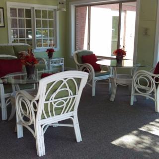 A sunlit indoor seating area with white chairs and tables, decorated with red cushions and flower arrangements.