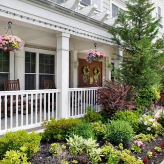 A charming front porch surrounded by a well-maintained garden with colorful flowers and hanging baskets.