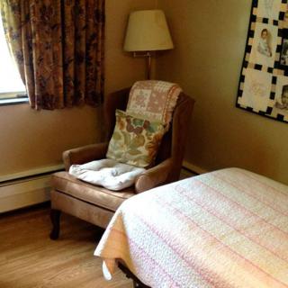 A cozy bedroom corner featuring a comfortable armchair and a quilt-covered bed.