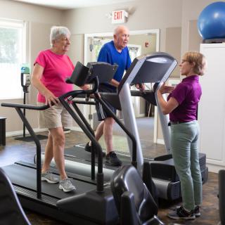 Seniors exercising on treadmills with a trainer in a fitness center.