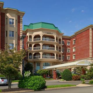 A grand hotel building with a green roof, surrounded by trees and a well-maintained garden.