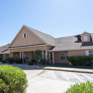 A suburban residential building with a sloped roof and front yard greenery under a clear blue sky.