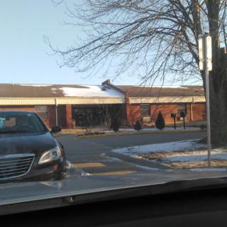 A view of a brick building during winter, with snow on the ground and a parked car in the foreground.