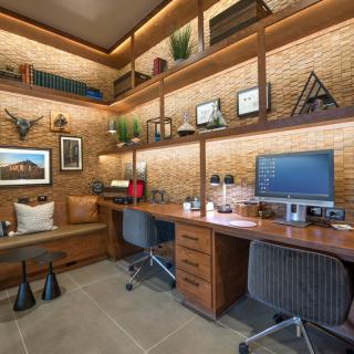 A modern office workspace featuring a wooden desk, computer setup, and decorative shelves on a brick wall.