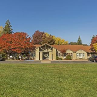 A picturesque building surrounded by colorful autumn trees and a large green lawn under a clear blue sky.