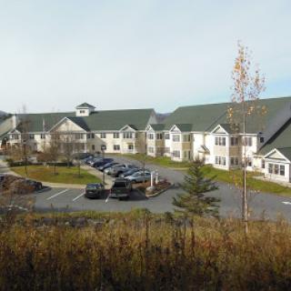 A suburban residential building with a parking lot and surrounding trees.