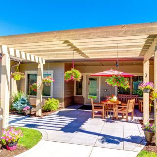 A sunny patio area with a wooden pergola, outdoor furniture, and hanging plants.