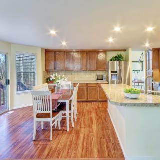 A modern kitchen with wooden floors, featuring a dining area and island counter under bright lighting.