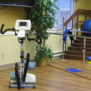 A physical therapy room featuring an exercise bike, balance bars, and stairs.