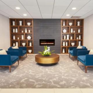 A modern lobby with blue seating, a central round table, and a stylish fireplace surrounded by decorative shelves.