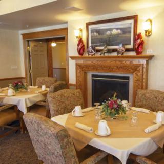 A cozy dining room with round tables, upholstered chairs, and a decorative fireplace.