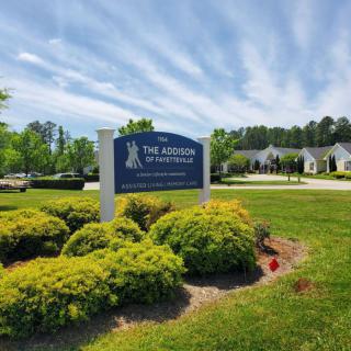 A landscape view featuring a sign for The Arbors Apartments with well-maintained greenery and a cloudy sky in the background.