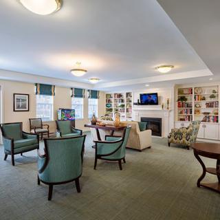 A spacious and well-lit living room with comfortable seating, tables, a fireplace, bookshelves, and a television.