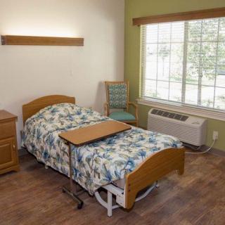 A hospital room featuring a single bed, bedside table, and large window.