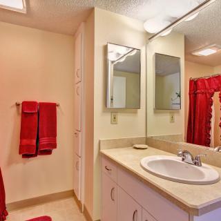 A bright bathroom featuring a sink with a large mirror above it, accompanied by red towels and shower curtain.
