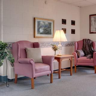 A cozy living room with two pink armchairs, a lamp, and wall decor.