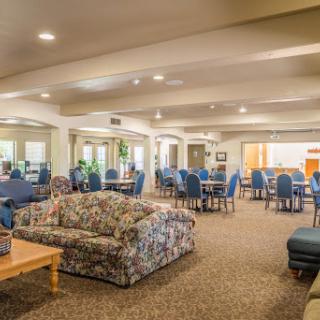 A spacious lounge area featuring a cozy floral sofa, dining tables, and blue chairs under warm lighting.