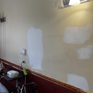 A partially painted wall showing patches of white paint over a beige background, indicating ongoing renovation work.