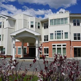 A modern residential building surrounded by colorful flowers under a bright blue sky.