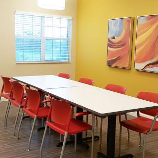A bright conference room with a long table and vibrant orange chairs against yellow walls.