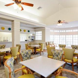 A bright and spacious dining area with multiple tables, chairs, ceiling fans, and large windows.