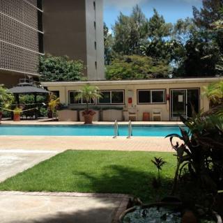 A serene outdoor swimming pool area surrounded by green plants and buildings.