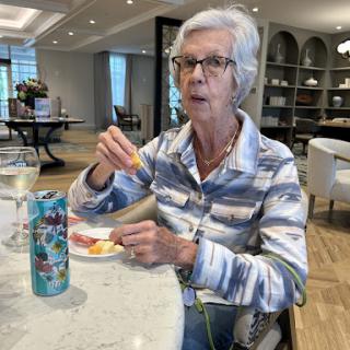 An elderly woman enjoying her meal and drink in a cozy dining setting.