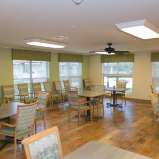 A spacious dining area with multiple tables and chairs, large windows, and wooden flooring.