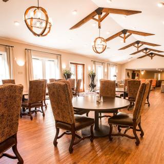 A warmly lit dining area with wooden floors, large chairs, and decorative lighting fixtures.