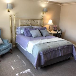 A cozy bedroom with a neatly made bed, an armchair, and a bedside table lamp.