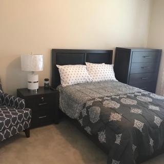 A cozy bedroom featuring a neatly made bed, a small dresser, and a patterned armchair.