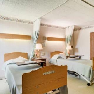 A hospital room with two beds separated by curtains, featuring bedside tables and lamps.