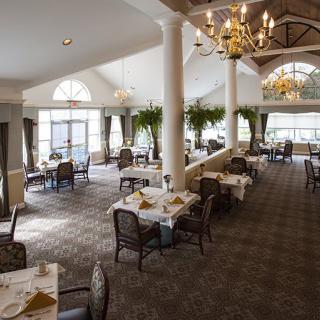 A spacious and elegant dining area with chandeliers, natural lighting, and neatly arranged tables and chairs.