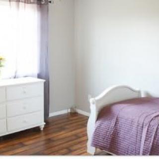 A minimalist bedroom with a white dresser, single bed, and hardwood flooring.