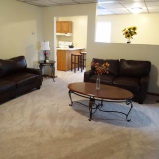 A cozy living room with dark sofas, a wooden coffee table, and a view into the kitchen.