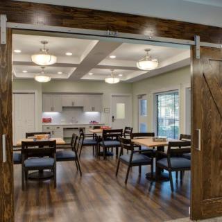 A modern dining area with wooden floors, contemporary lighting, and a kitchen in the background.