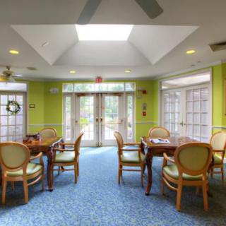 A brightly lit dining area with several tables and chairs, featuring a skylight and large windows.