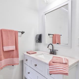A tidy bathroom with pink towels and a large mirror above the sink.