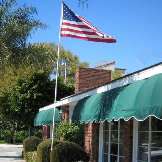 An American flag waves in front of a building with green awnings on a clear day.