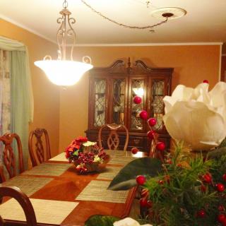 A warmly lit dining room with a large wooden table, ornate chandelier, and decorative floral arrangements.