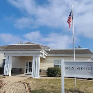 A business office building with an American flag in front, set against a cloudy sky.