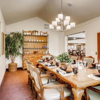A cozy dining room with a large wooden table and elegant chairs, adorned with a chandelier and surrounded by tasteful decor and plants.
