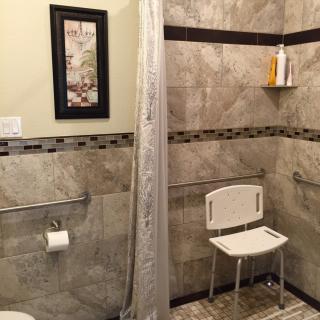 A modern bathroom with tiled walls, featuring a shower with a curtain and a shower chair.