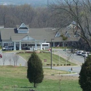 A building with a driveway, surrounded by trees and a parking lot.