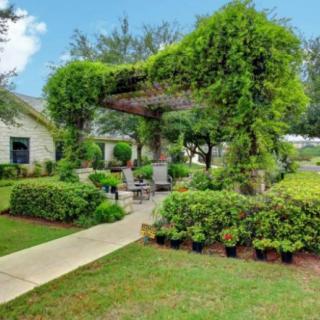 A beautifully landscaped garden featuring a pergola covered with lush greenery and surrounded by well-maintained shrubs and a paved pathway.