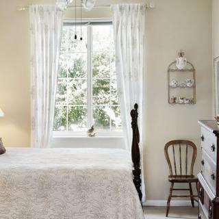 A cozy vintage-style bedroom with natural light pouring through a window framed by white curtains.