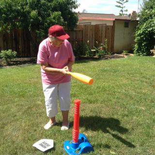 A person playing tee ball in the backyard, preparing to hit a ball with a plastic bat.