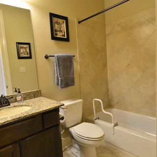 A well-appointed bathroom featuring a bathtub with a grab bar, a toilet, a sink with countertop space, and decorative elements like framed pictures and a towel rack.